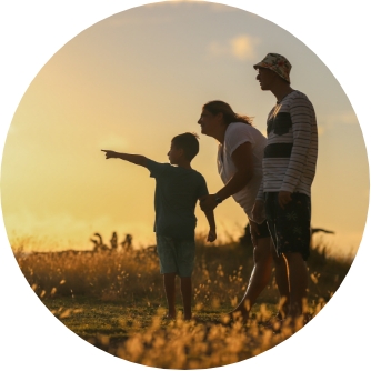 A child is pointing on a warm summer's evening to something in the distance while two origins foster carers look in that direction.