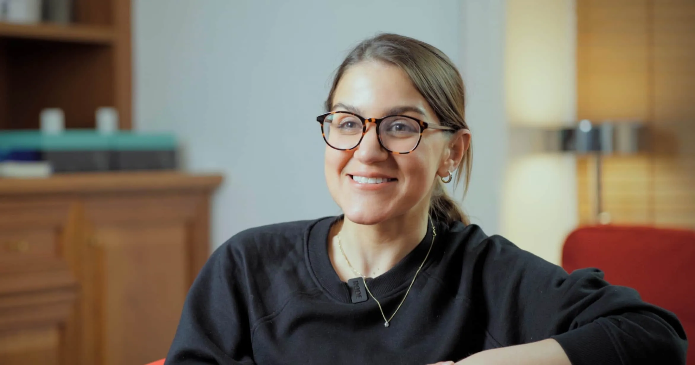 Zahra a Senior Practitioner and Link Social Worker at Origins Foster Care smiling with a pair of glasses on in the Origins office.