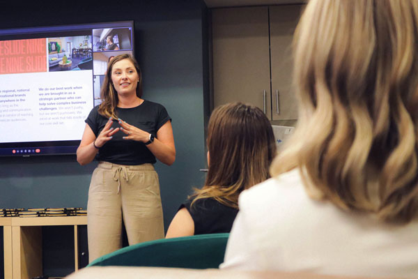 Slide Nine employees engaged in listening to a presentation being given by their CEO, Lauren Parker