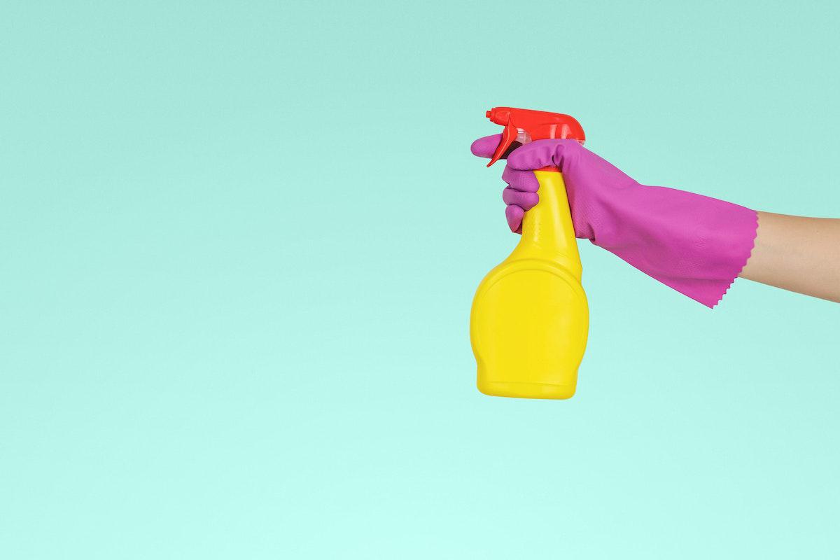 Hand wearing pink rubber glove holding cleaning spray