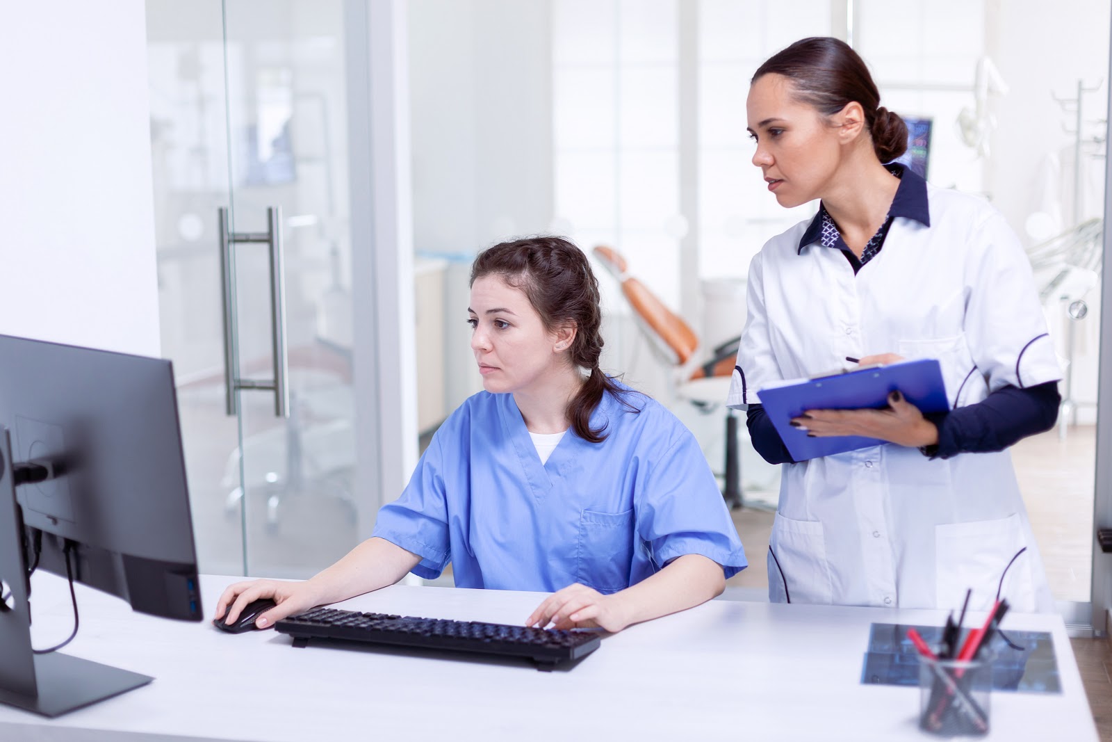 dentist and office manager review patient records on their desktop computer