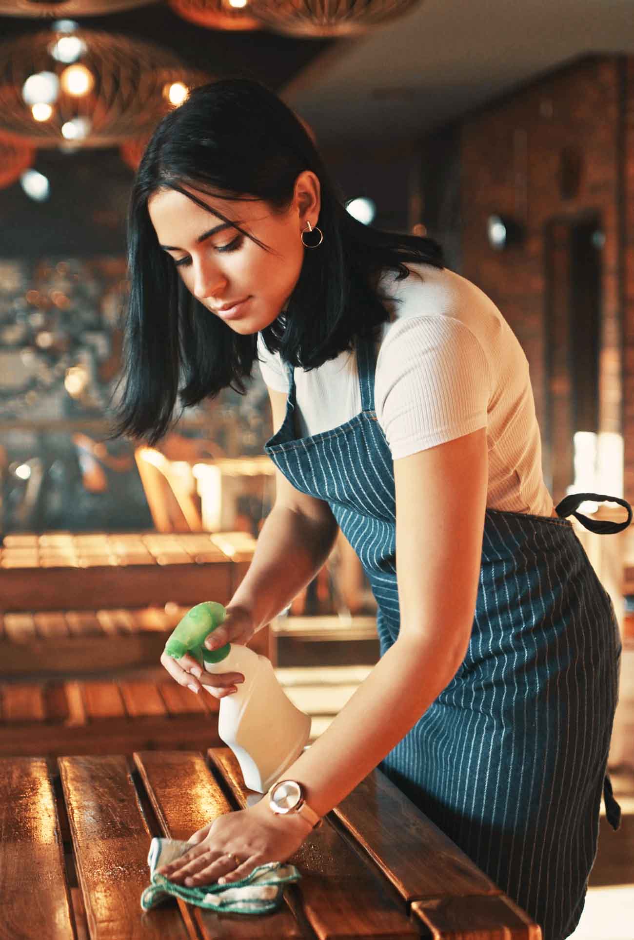 A woman wearing an apron who is cleaning a table
