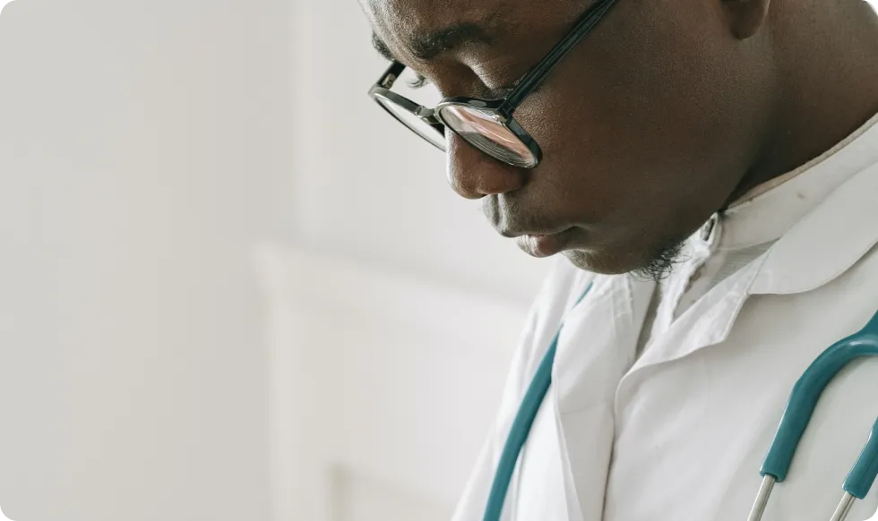 A male doctor standing with glasses facing down.