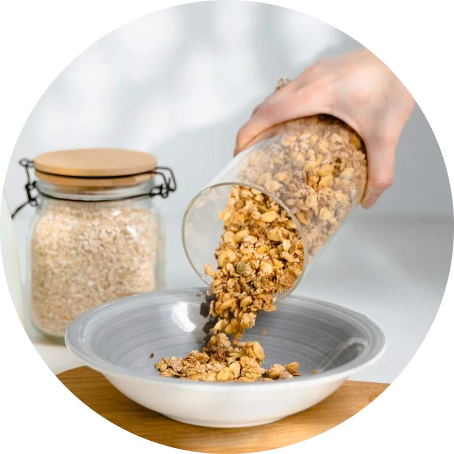 A female hand holding a glass pouring nuts on a bowl that's on a table with a closed glass jar full of pounded nuts.