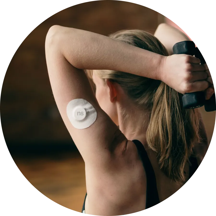A back view of a lady holding dumbbell on both hands towards her back wearing Nutrisense cgm sensor on her left upper hand.