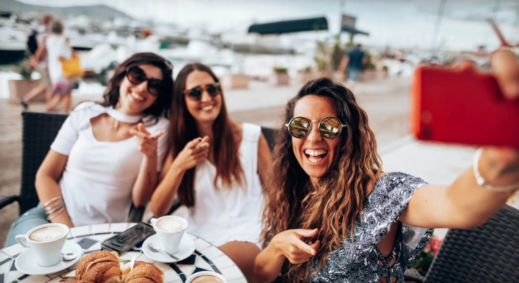 Smiling millennial takes a selfie with two friends at a table outside a cafe