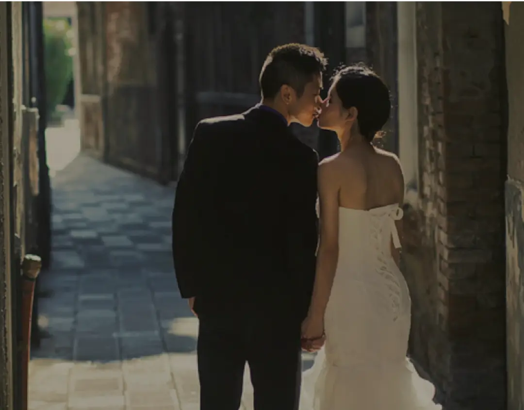 Newlyweds kiss while holding hands.