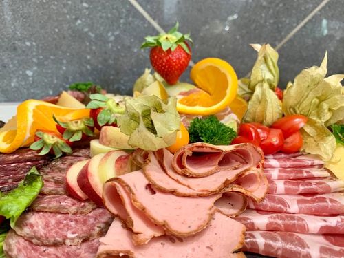 Eine Platte mit vielen Köstlichkeiten des Hofladens versehen. Man sieht verschiedene Wurstsorten und schön angerichtet mit Obst.