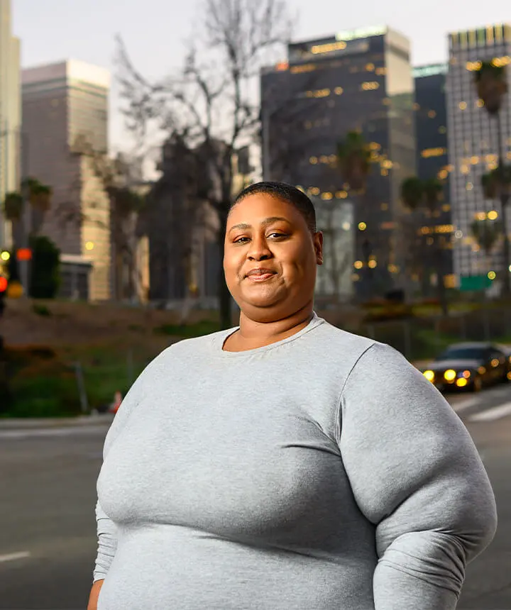 Portrait of a black woman wearing a gray shirt in front of a city skyline