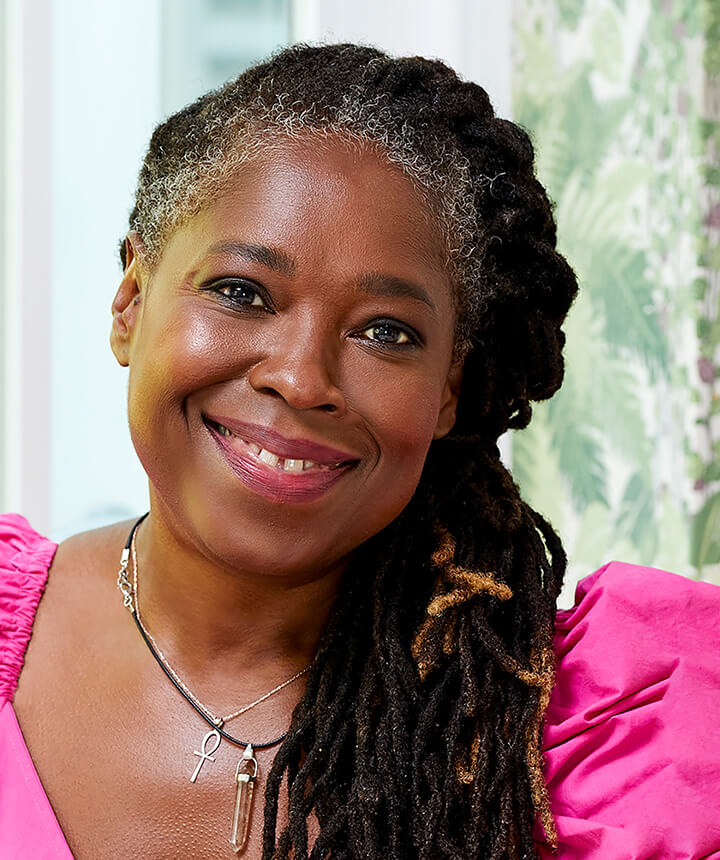 An older Black woman with some grey hair, wearing a pink dress and smiling brightly