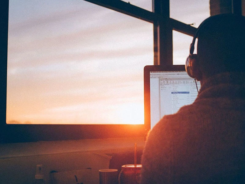 Teen sitting at his computer doing online therapy as the sun sets