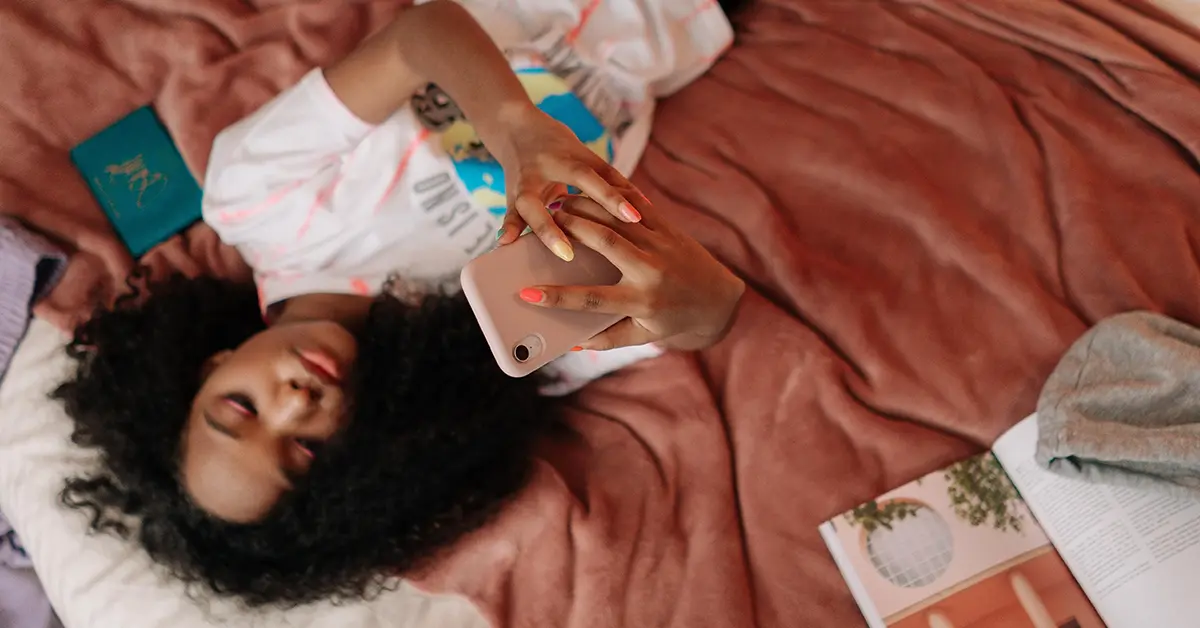 A teen lays in bed alone on her phone