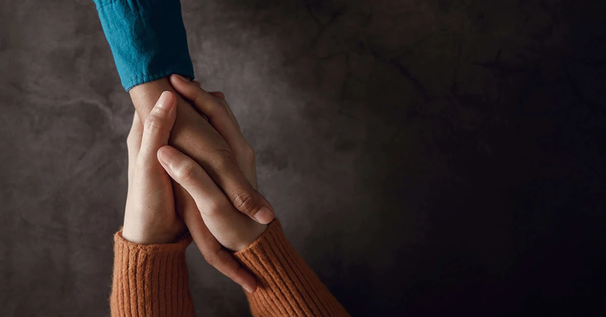Two individuals holding hands while one individual provides support