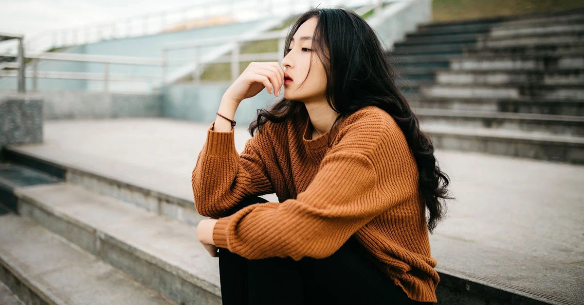 A teen in a brown sweater sits on bleachers, looking sad