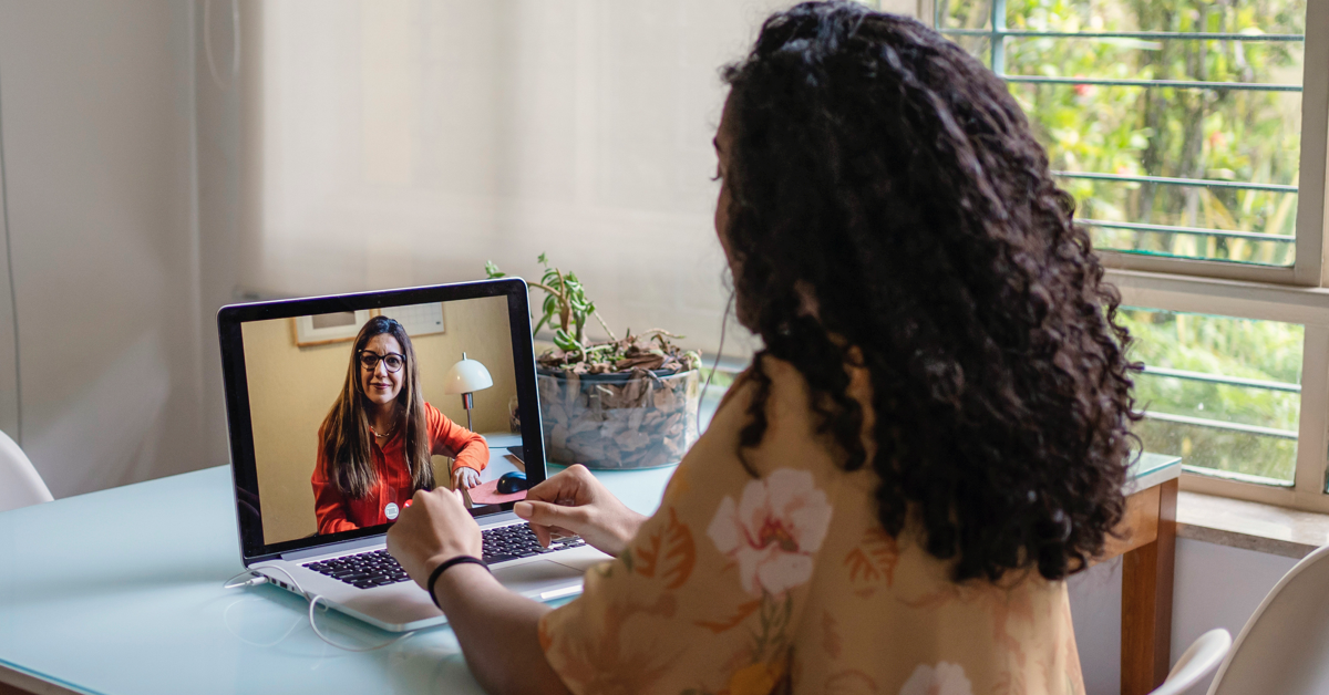 A young person of color receives teletherapy at home from a therapist of color.