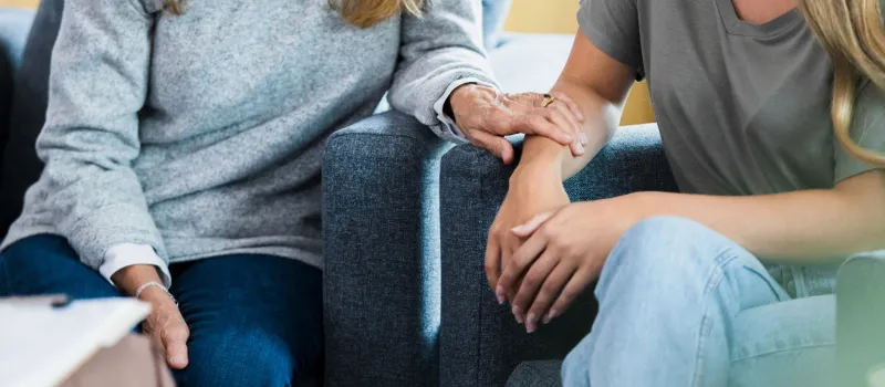 A mom in a gray sweater sits with her daughter with blonde hair in a family therapy session