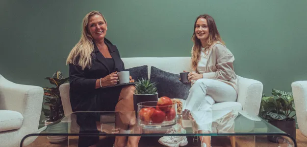 Alexandra og Monika som sitter i en sofa og smiler til kamera