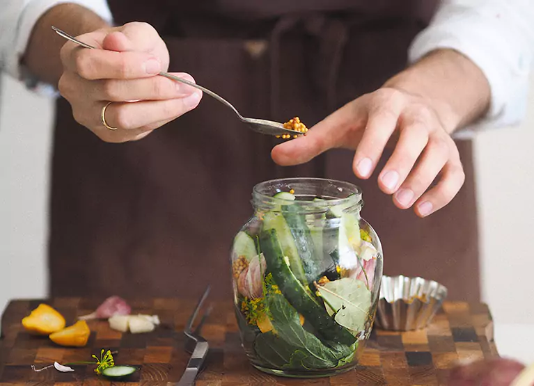 someone adding cucumbers into a jar with spices