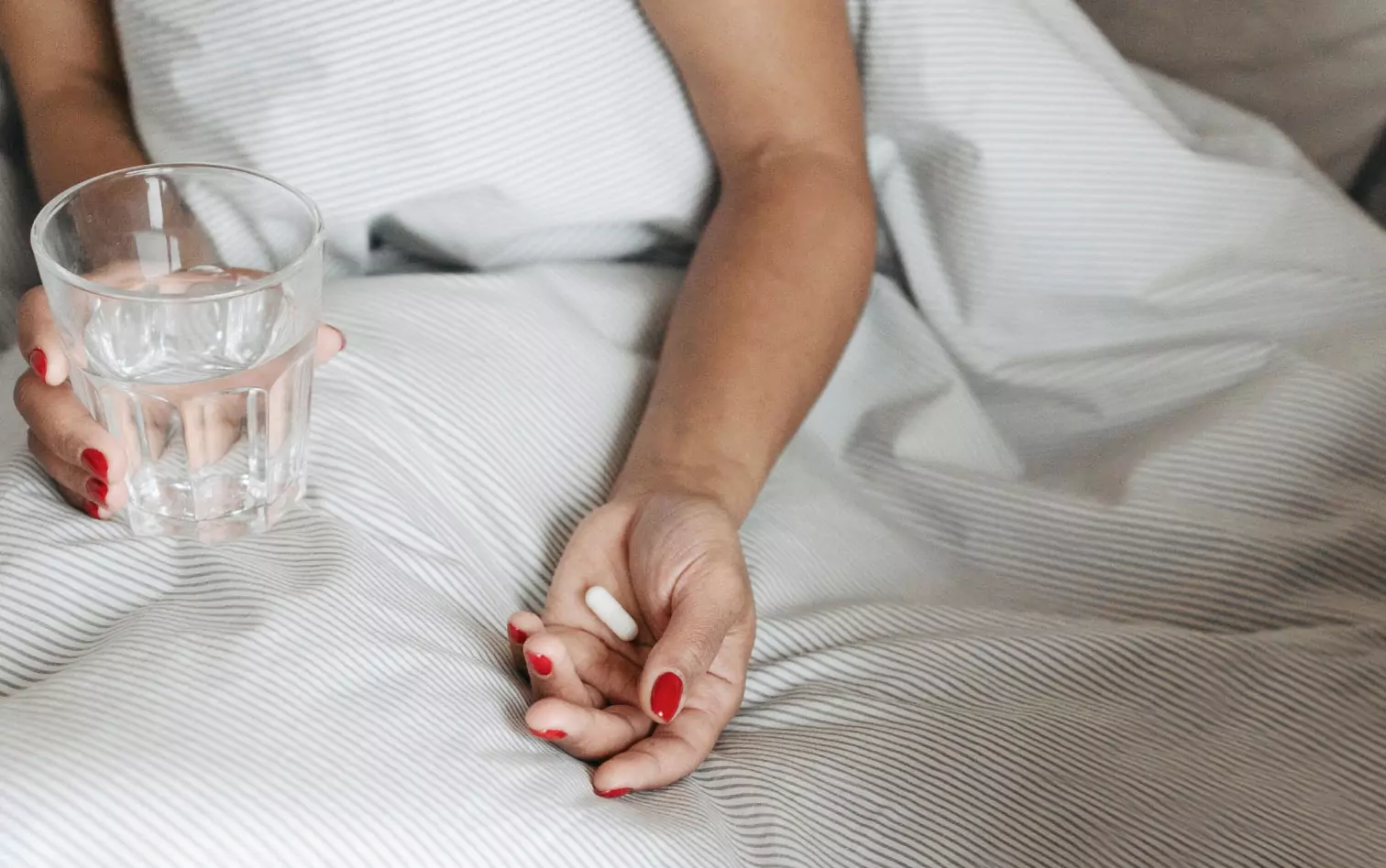 a woman holding glass of water in one hand and a pill in the other
