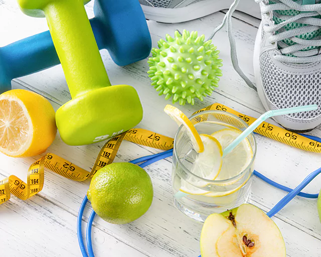 a glass of water with lemon, dumbbells, tape measure and sneakers