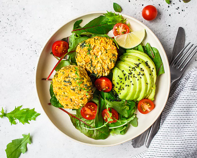 a plate of cut avocado, tomatoes and green leafy vegetables