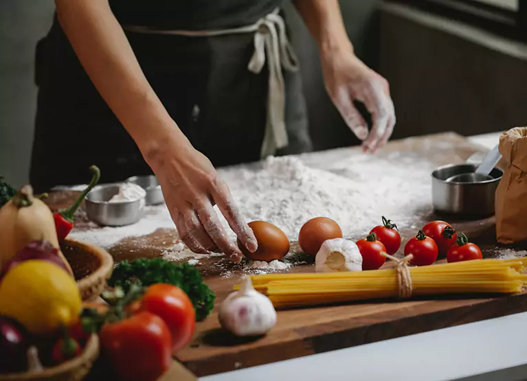 Wooden kitchen counter with eggs, tomatoes, pasta, chillies, and flour