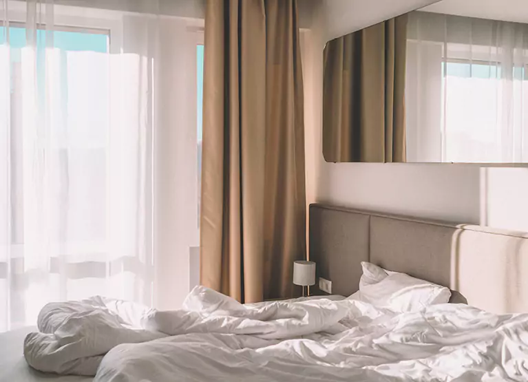 Bedroom with white linen bed and a large window that has sunlight streaming in
