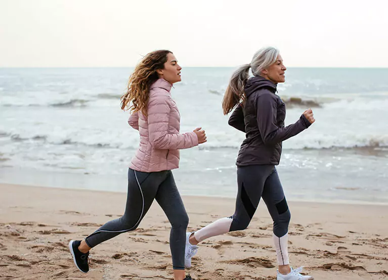 A young woman and an older woman running together on the beach