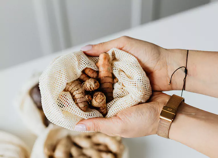 Person's palm holding white mesh bag with fresh turmeric root