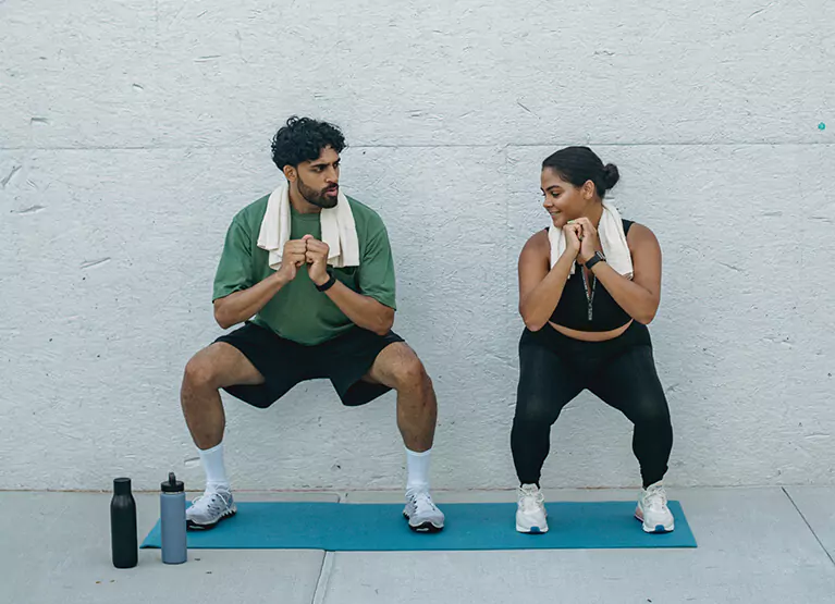 A man and woman doing squats on yoga mat