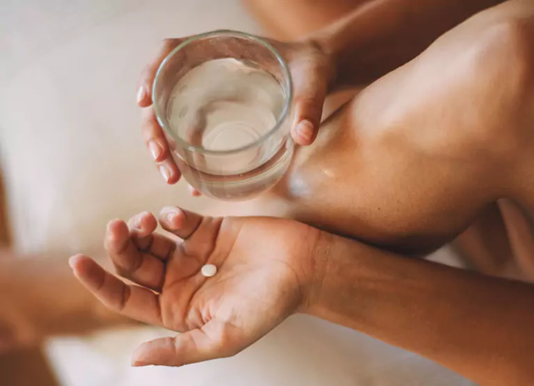 Person holding anti-anxiety pill in one hand with glass of water in other