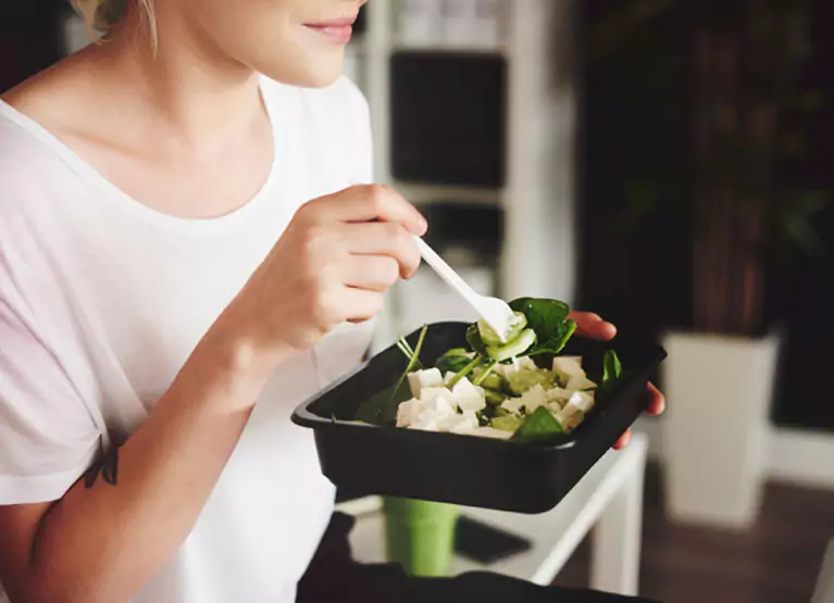 a woman eating a salad out of a tupperware
