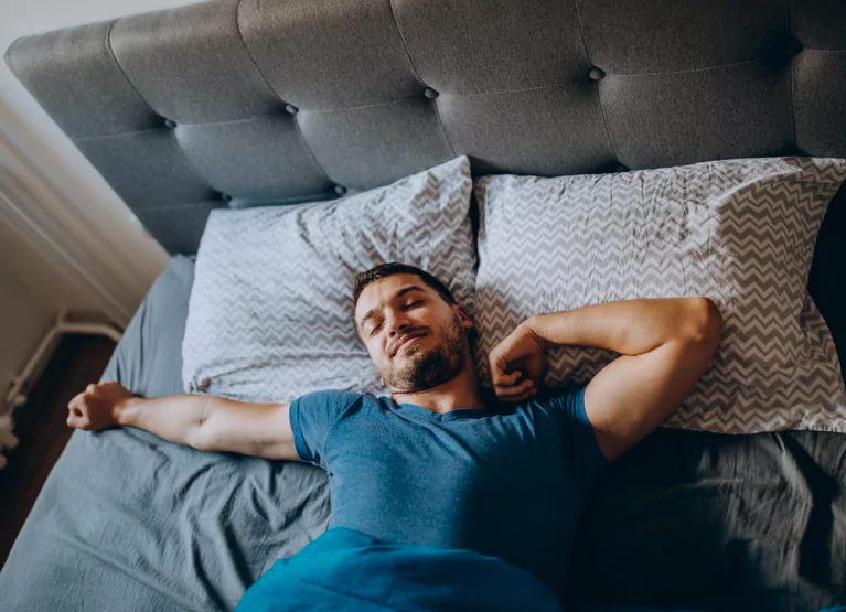 Man laying and stretching on gray bed with tufted headboard