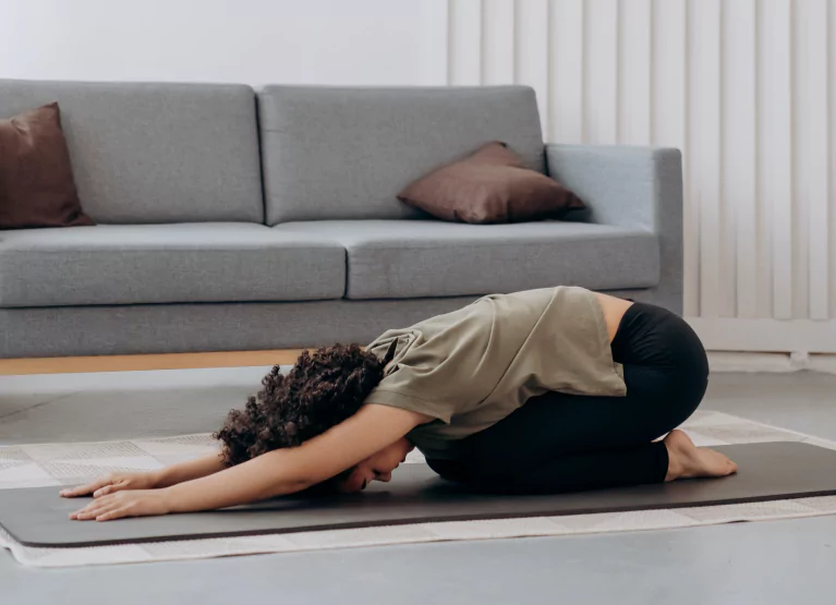 Woman stretching on black yoga mat by living room couch