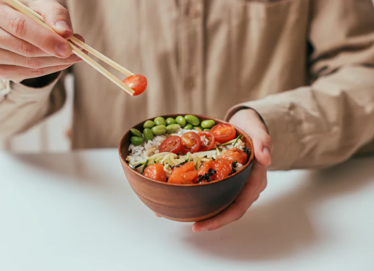 someone using chopsticks to pick up a tomato in a bowl
