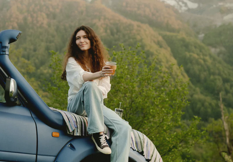 a girl sitting on a car with a drink