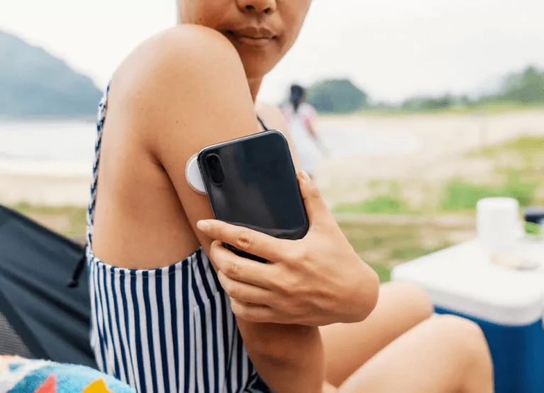Someone sitting outdoors scanning a continuous glucose monitor with a smartphone