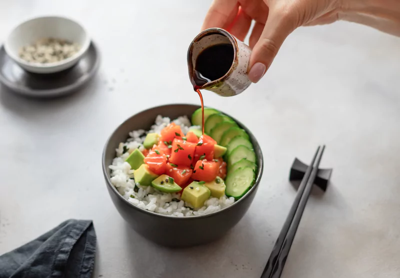 Person pouring soy sauce onto poke bowl