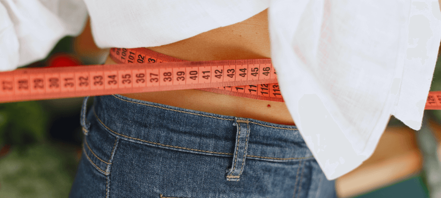 A closeup of someone checking their waist size with a measuring tape