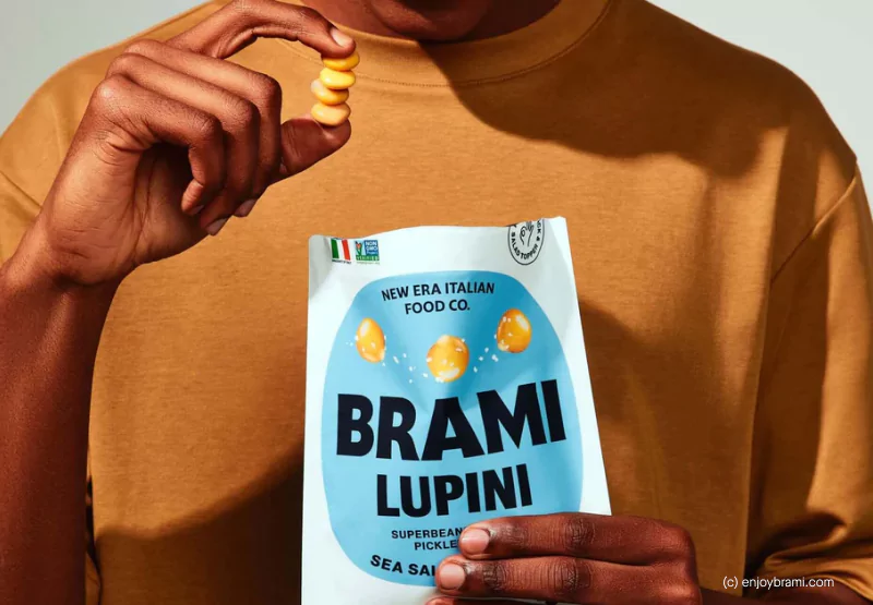 A closeup of someone in an orange t shirt holding a bag of Brami Lupini Beans