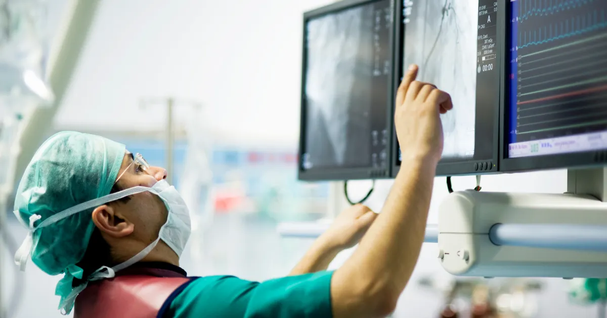 Surgeon pointing to imagery on a computer screen mounted to surgery equipment.
