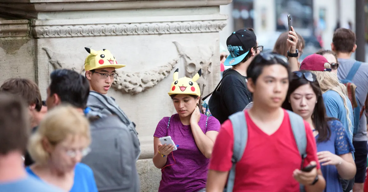 A man and a woman standing in a crowd wearing Pikachu hats and looking at their smartphones.