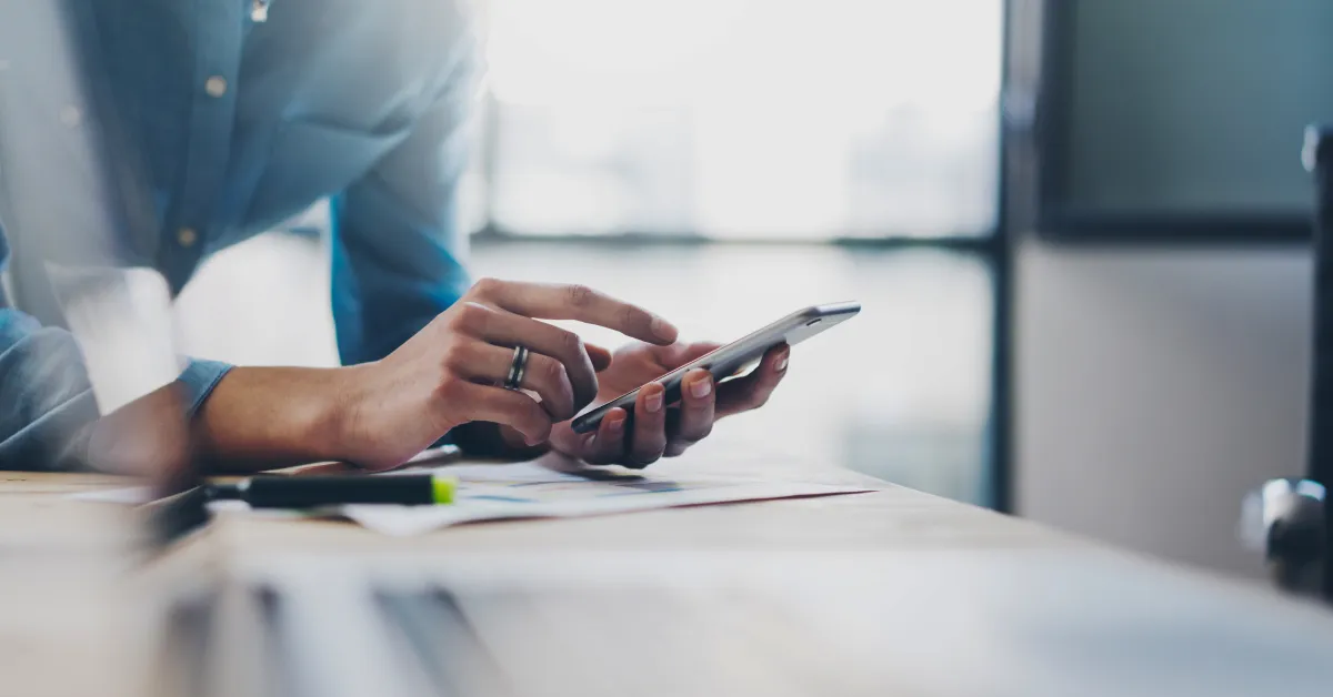 Man leaning on office desk browsing on his smartphone.