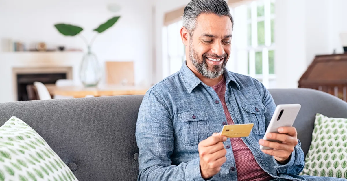 Man sitting on couch adding credit card information on his phone.