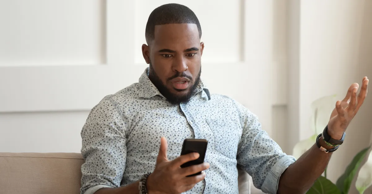Man sitting on couch looking frustratingly at smartphone.