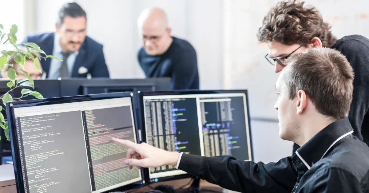 Two IT people discussing in discussion over computer code on display in front of them.