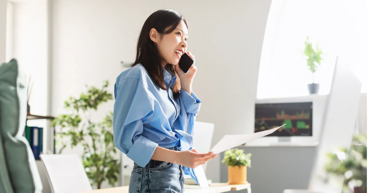 Women in a modern office talking on smartphone with office desk in background.