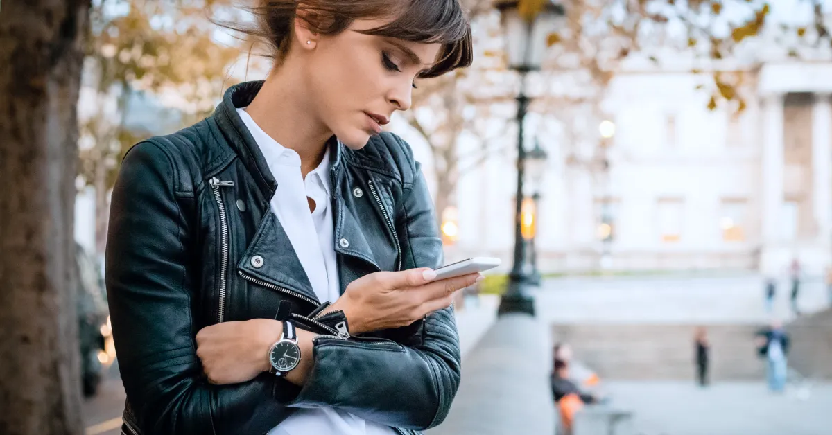 Women standing outside looking at smartphone.