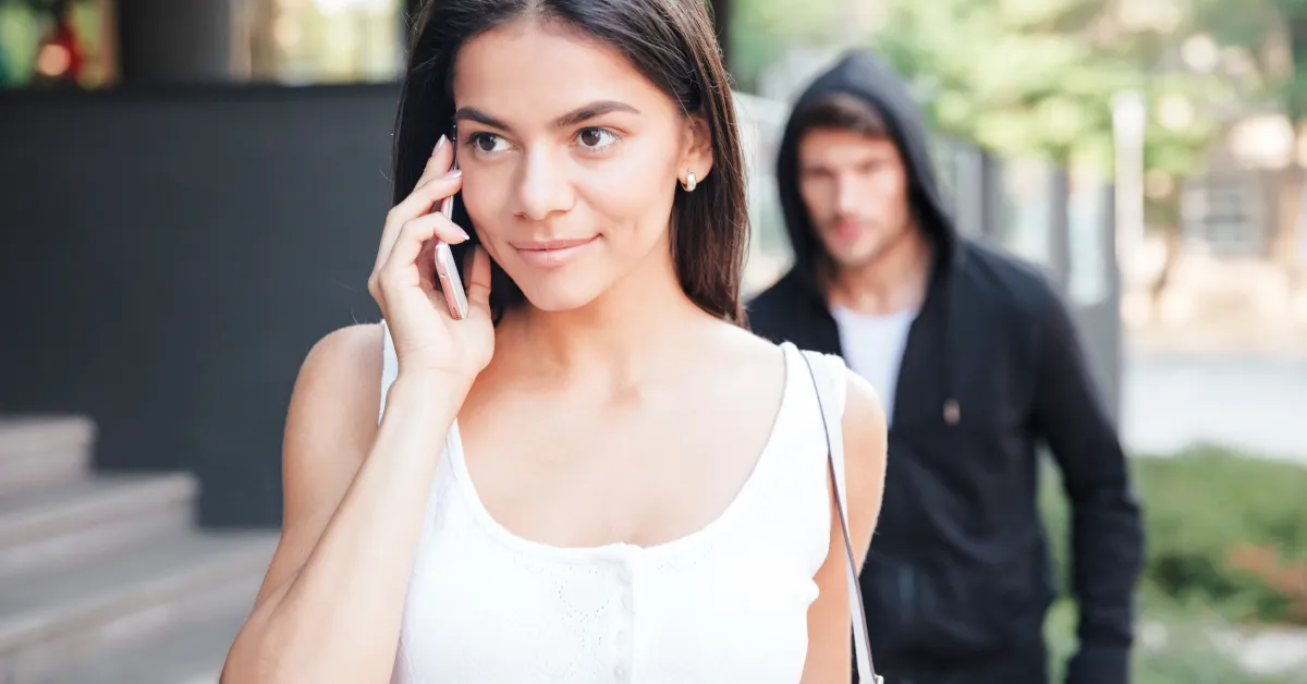 Women walking while talking on phone with ominous man following in the background.