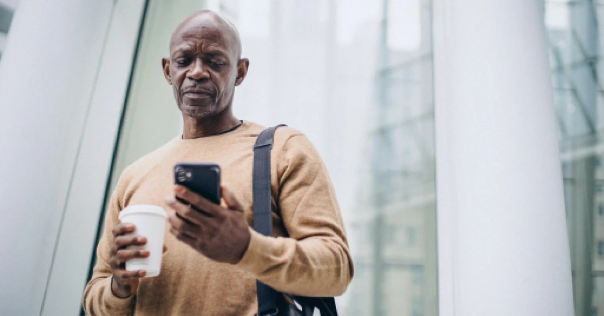 Focused man using smartphone during coffee break on street.